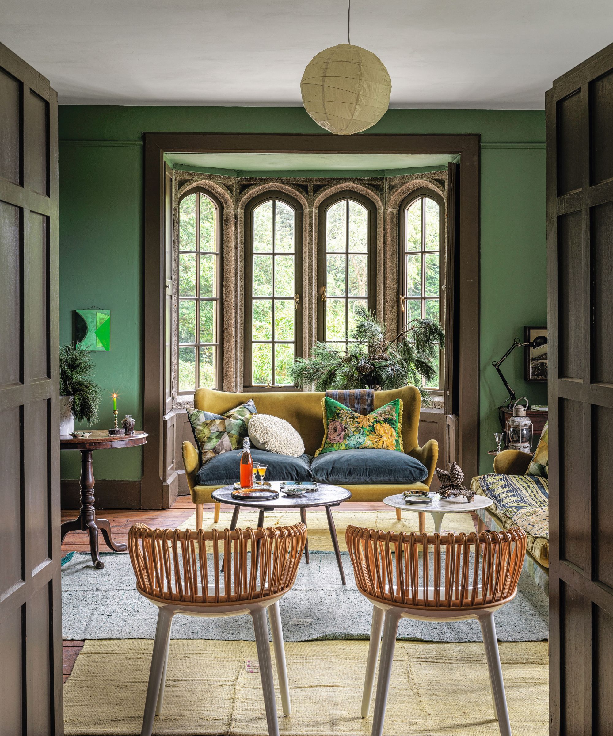 A green living room with large picture windows and eclectic furniture