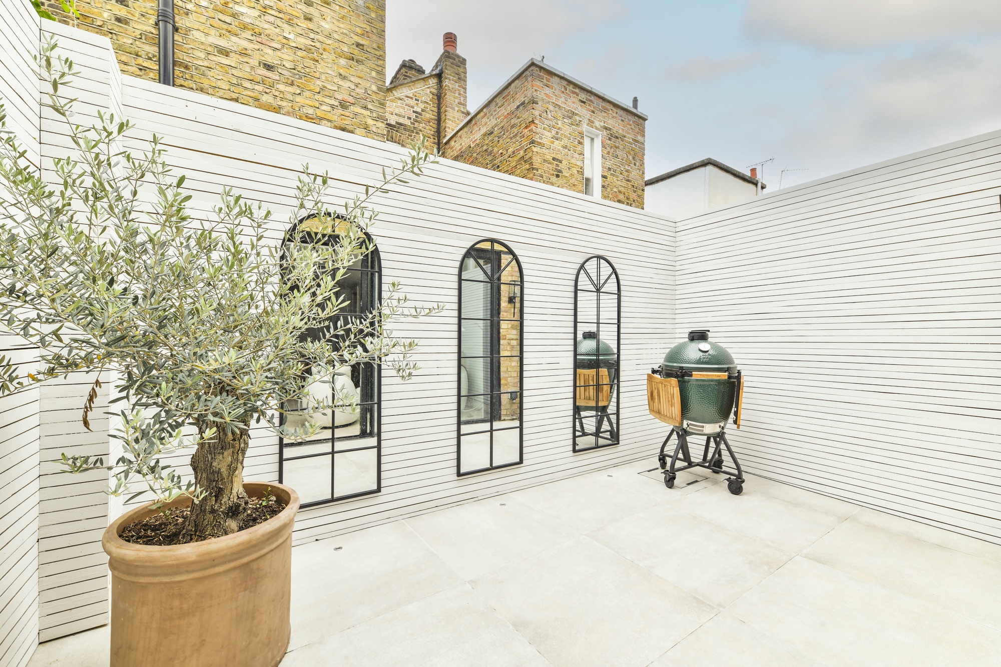 Courtyard garden with oversized arched mirrors and olive tree by Project London