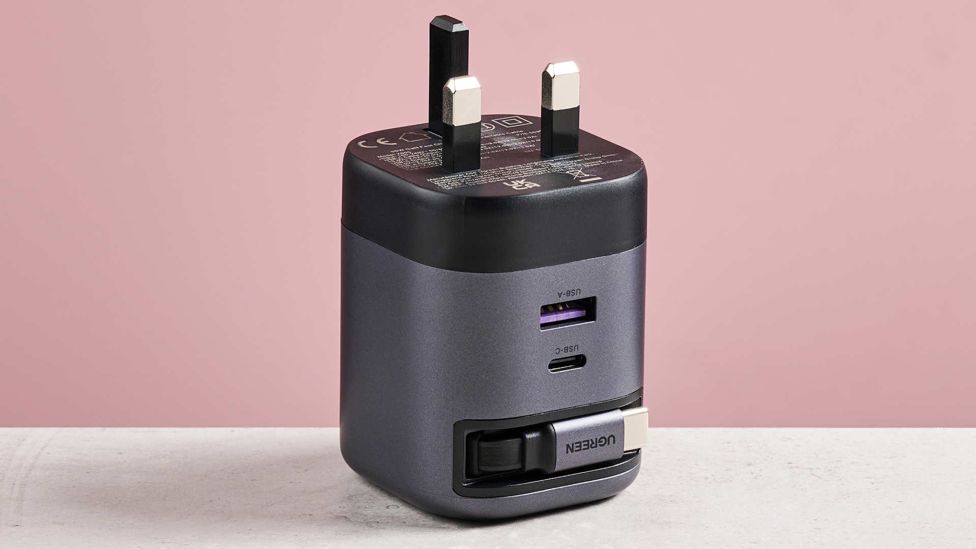 UGreen Nexode 65W Charger with Retractable USB-C Cable upside down on table against pink background