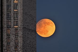 a shadow can be seen on the full moon in the sky as it sets behind buildings