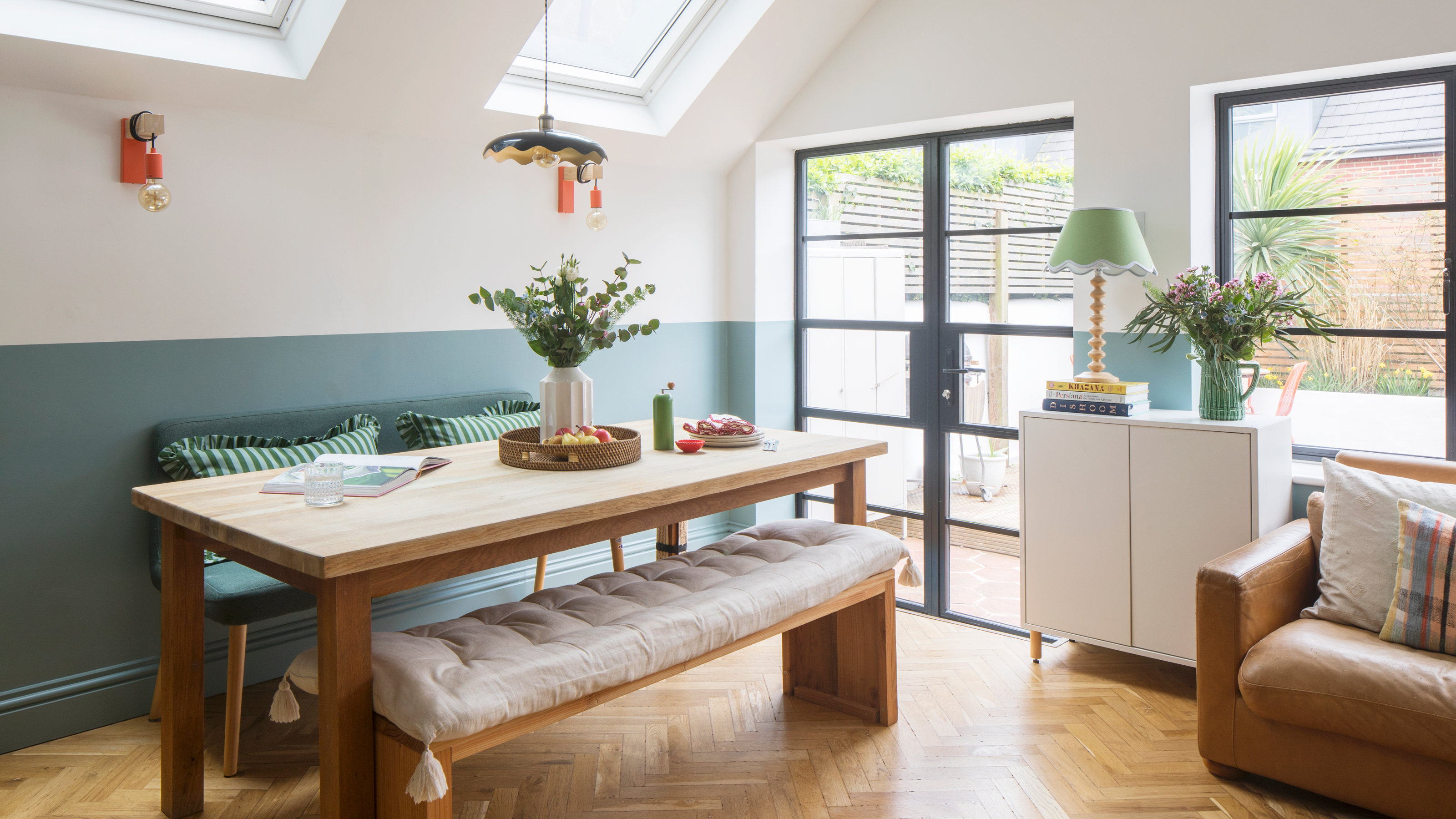a dining area that leads out to a garden via patio doors with a blue painted half wall and dining table and benches
