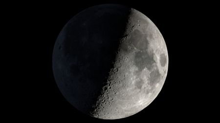 A graphic of the moon is pictured with its right half lit and its left in darkness against a black night sky.