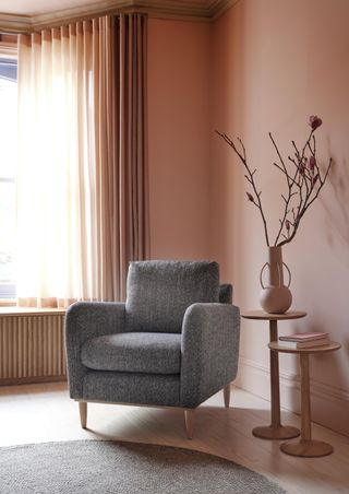 coral living room with grey armchair, vase on side table, pair of wooden side tables, gray round rug, coral drapes, wood panelled window seat
