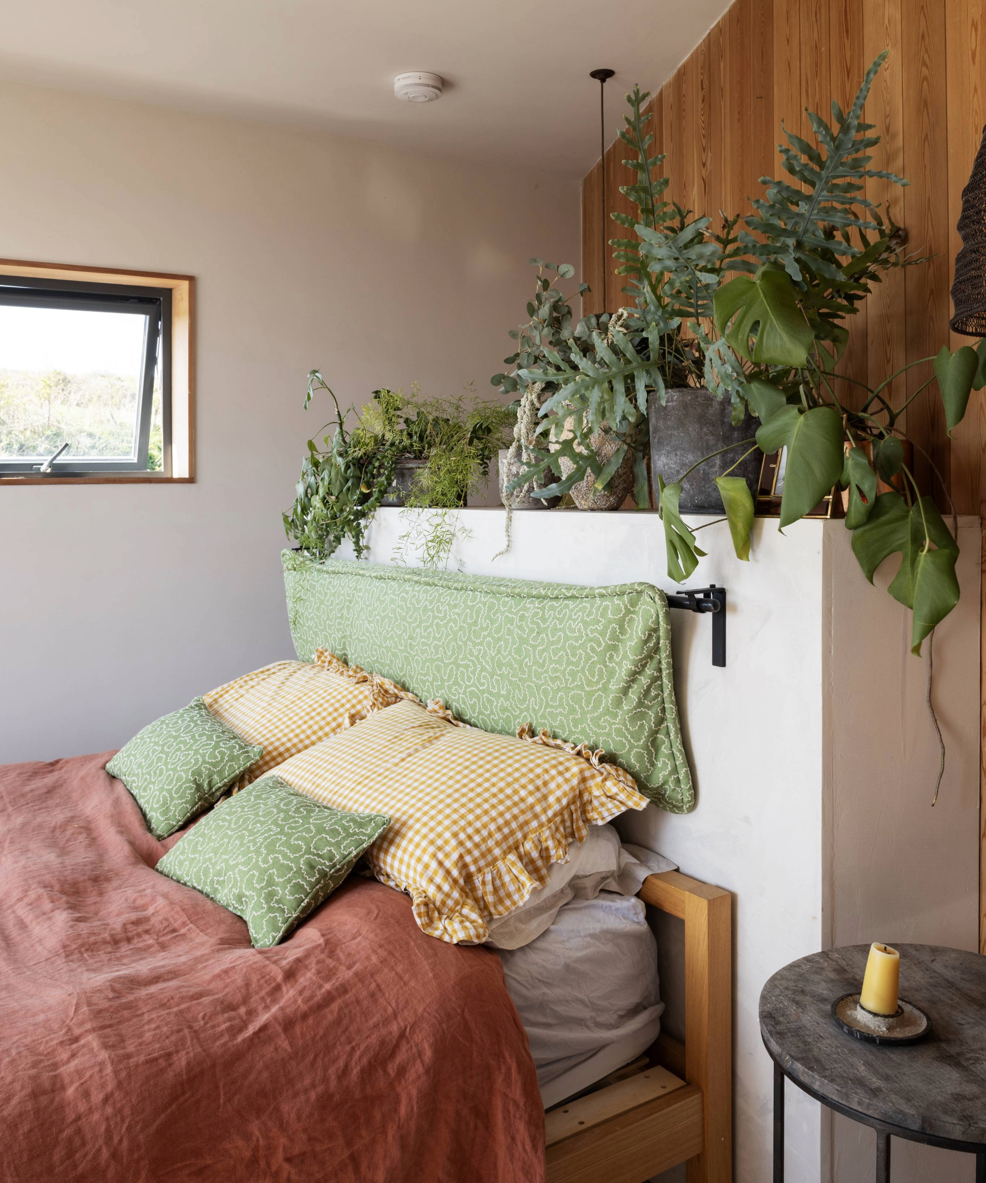 Bedroom with pink duvet, green and yellow cushionsm and plants on a white headboard
