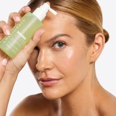 Middle-aged blonde woman holding Ameliorate skincare product to her face.