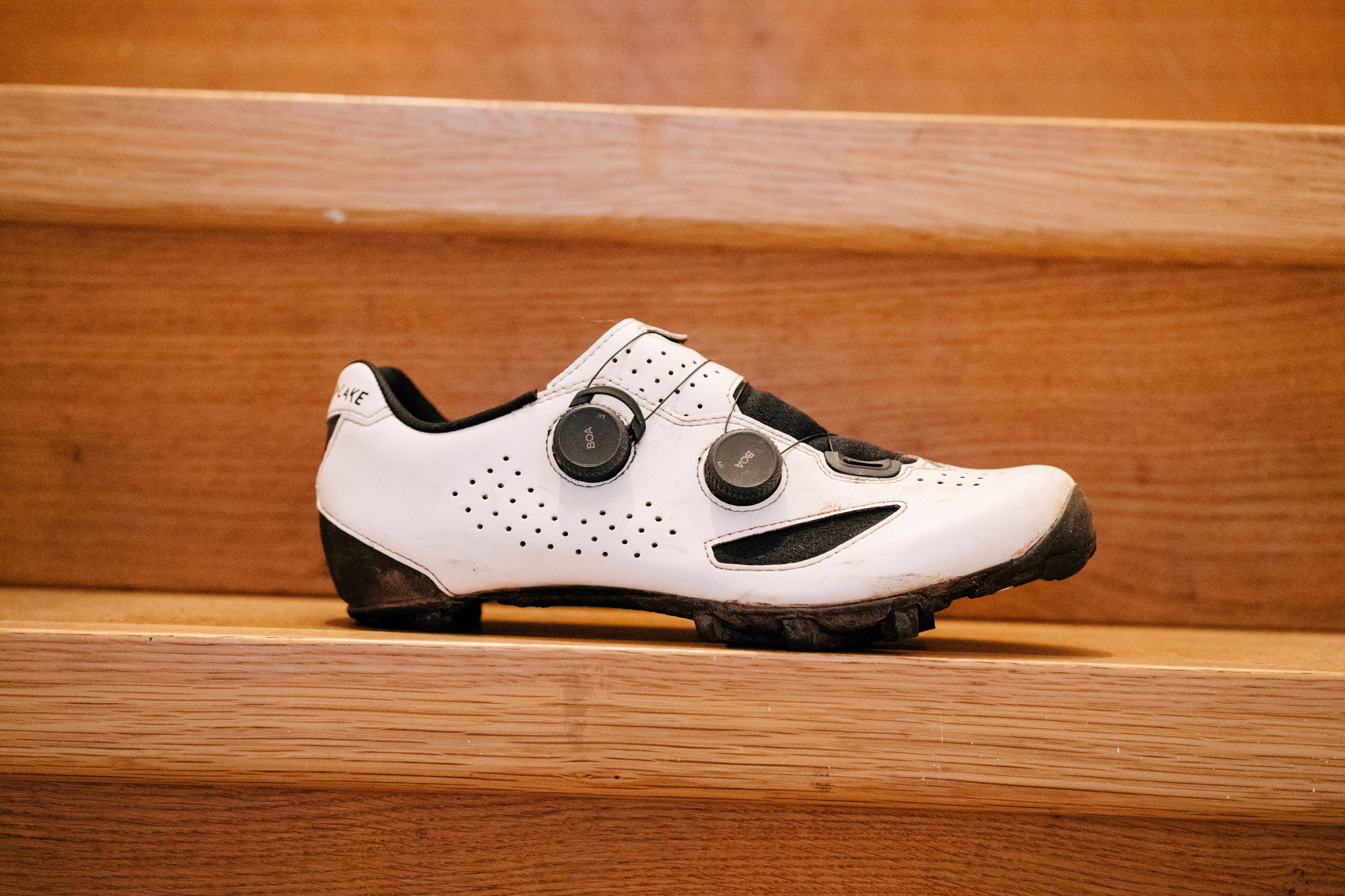 A white gravel bike shoe on wooden stairs