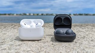 AirPods Pro 2 and Samsung Galaxy Earbuds 2 Pro side-by-side on a wall outside by a waterway