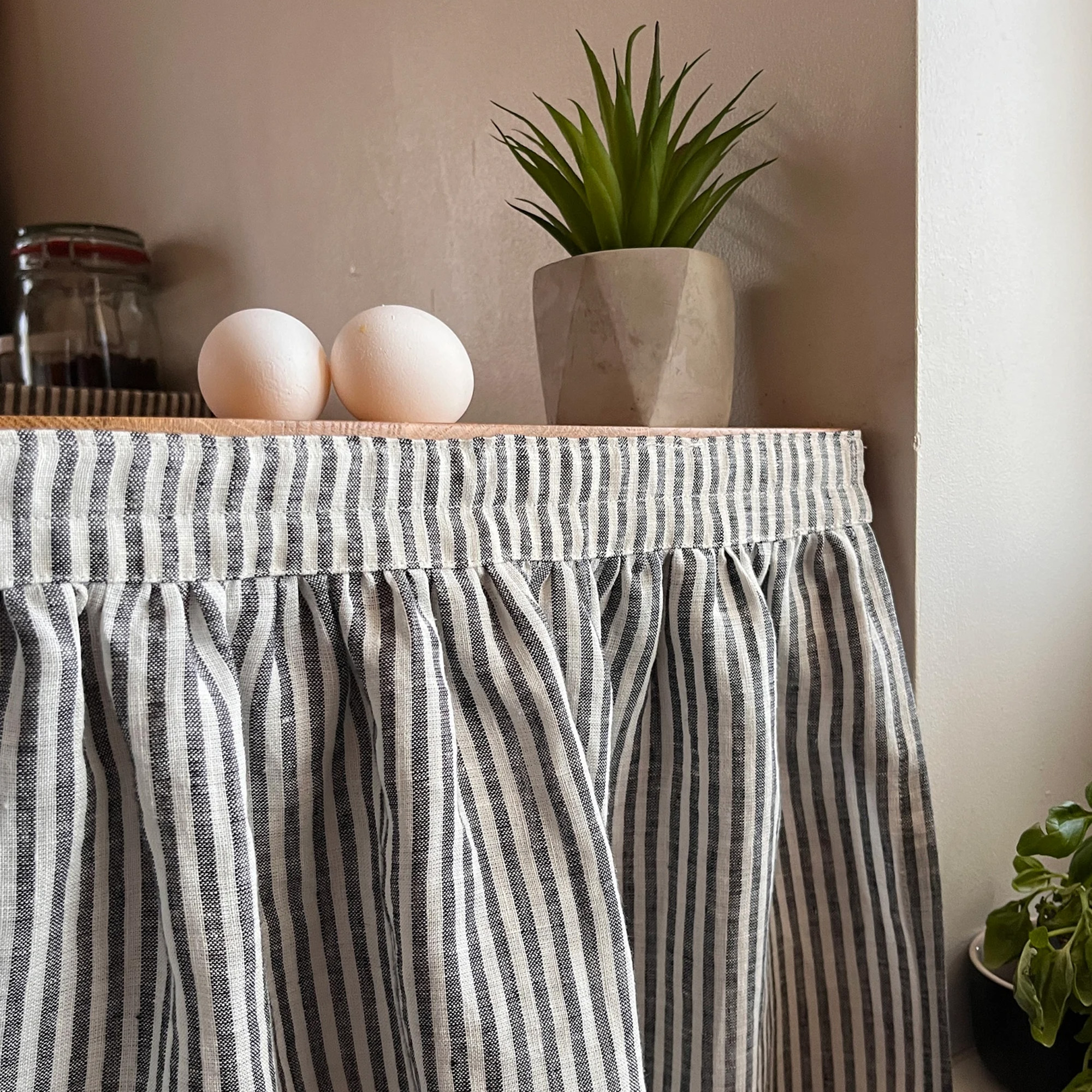 etsy sink skirt with black and white striped linen look across the front of a wooden unit with eggs and plant ontop 