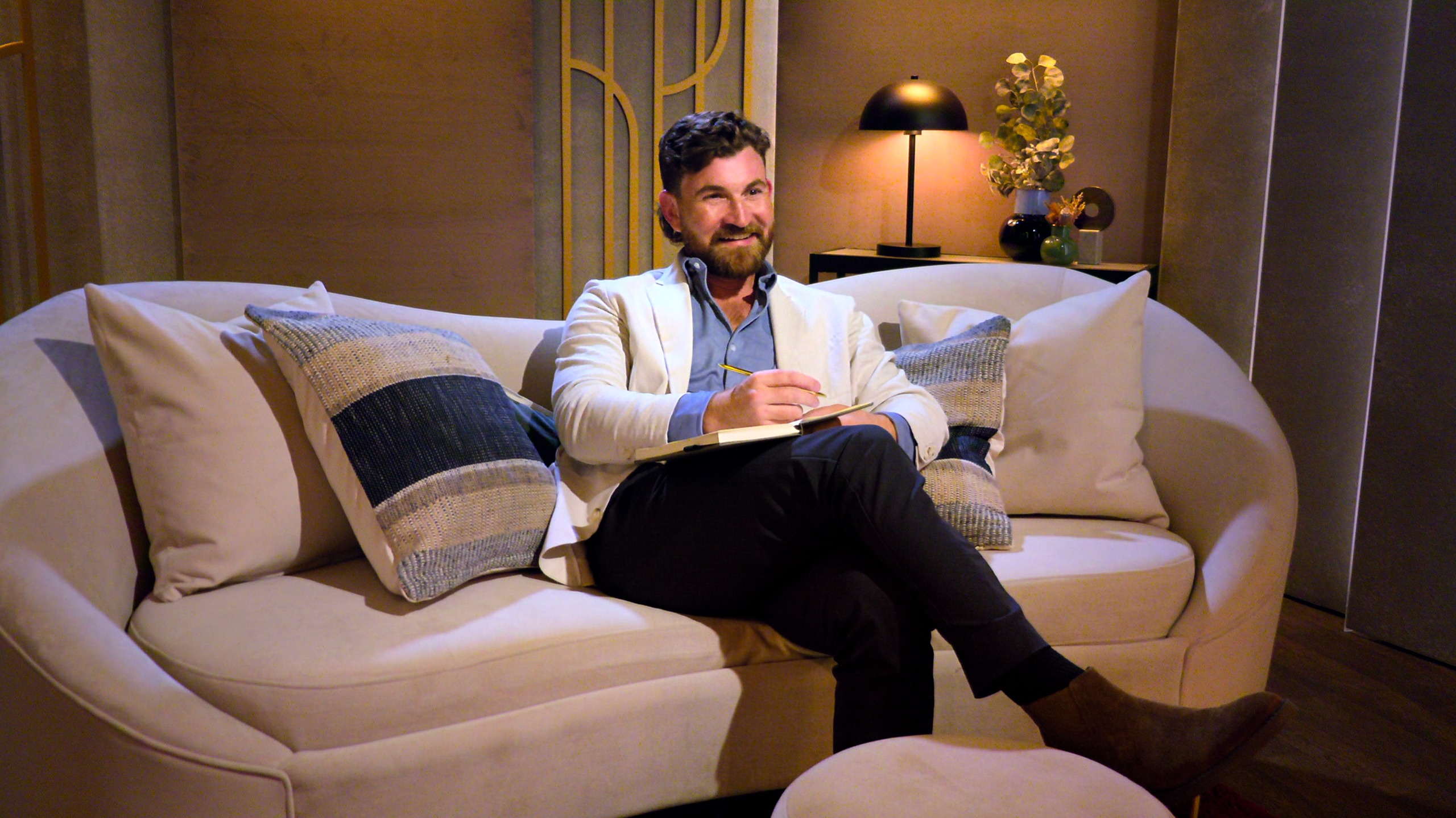 rob wearing a white blazer sitting on a sofa in the pods in love is blind season 11