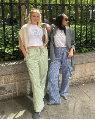 Fashion editors Yusra Siddiqui and Natalie Gray Herder pose on the sidewalk in New York City wearing striped-pajama-pant outfits.