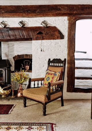 inglenook fireplace with rustic chair and stairs behind beams with limewashed walls