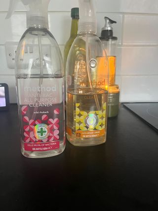 Two bottles of method cleaner, one pink and one yellow, a candle lit in the background