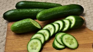 Four cucumbers on a chopping board, one of which has been sliced