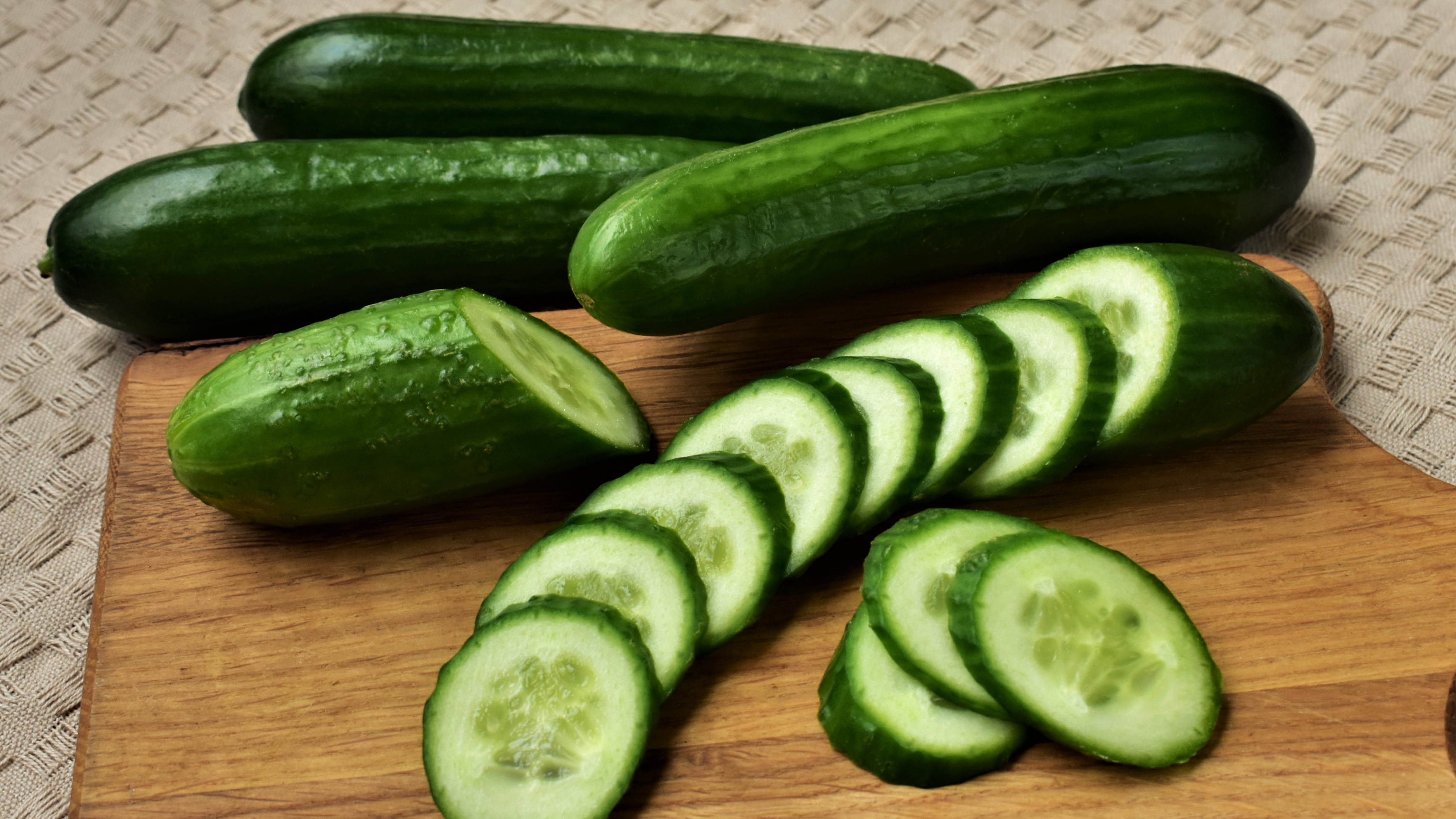Four cucumbers on a cutting board, one of which has been cut into slices