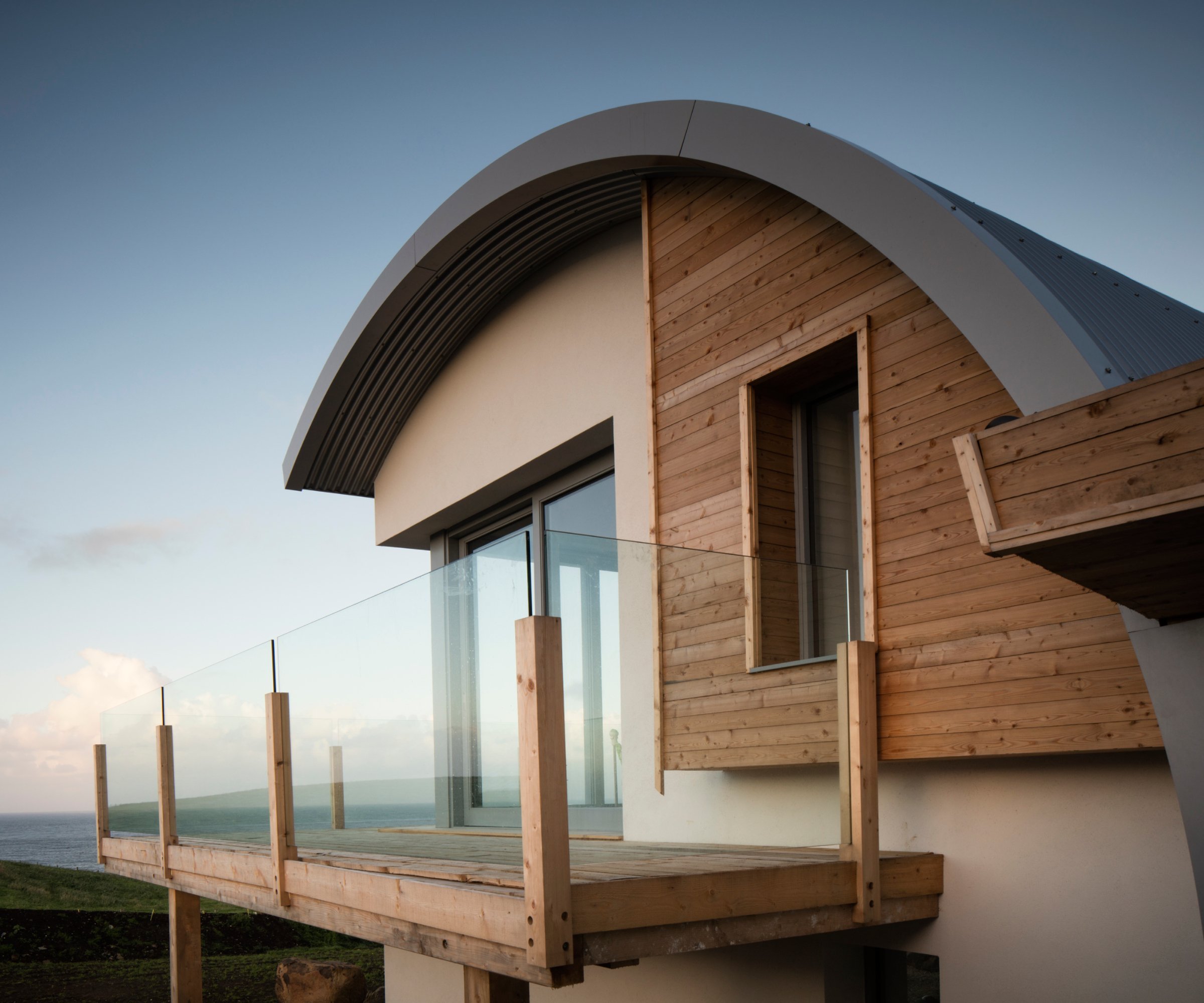 exterior of extension with curved metal roof, render and timber cladding on walls and balcony with timber and glass balustrade