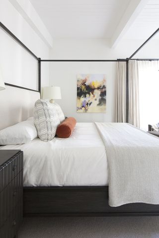 Melinda Mandell white bedroom with black bed, orange cushion and artwork