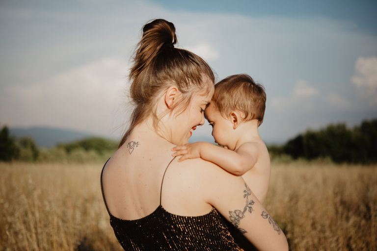 A mum with a tatto holding her baby in a field.