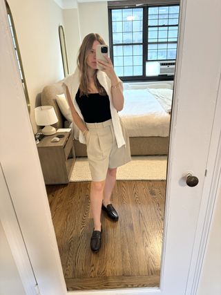 Nikki Chwatt wears Banana Republic's Lido bermuda shorts in beige with burgundy loafers, a black tank top, and white sweater.