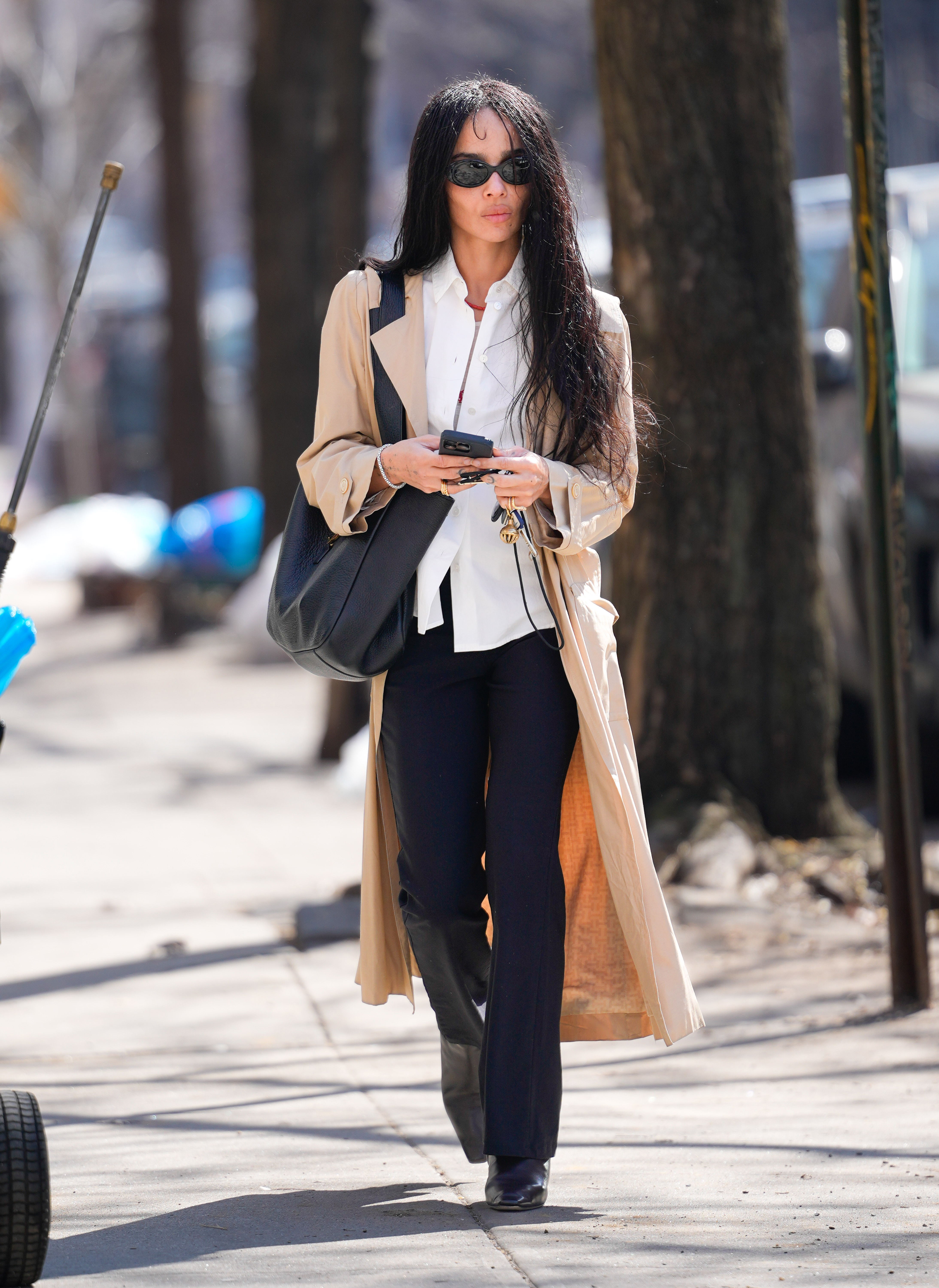 Zoe Kravitz walks down the streets in New York wearing a white shirt with bootcut trousers, square-toe boots and a beige trench coat.