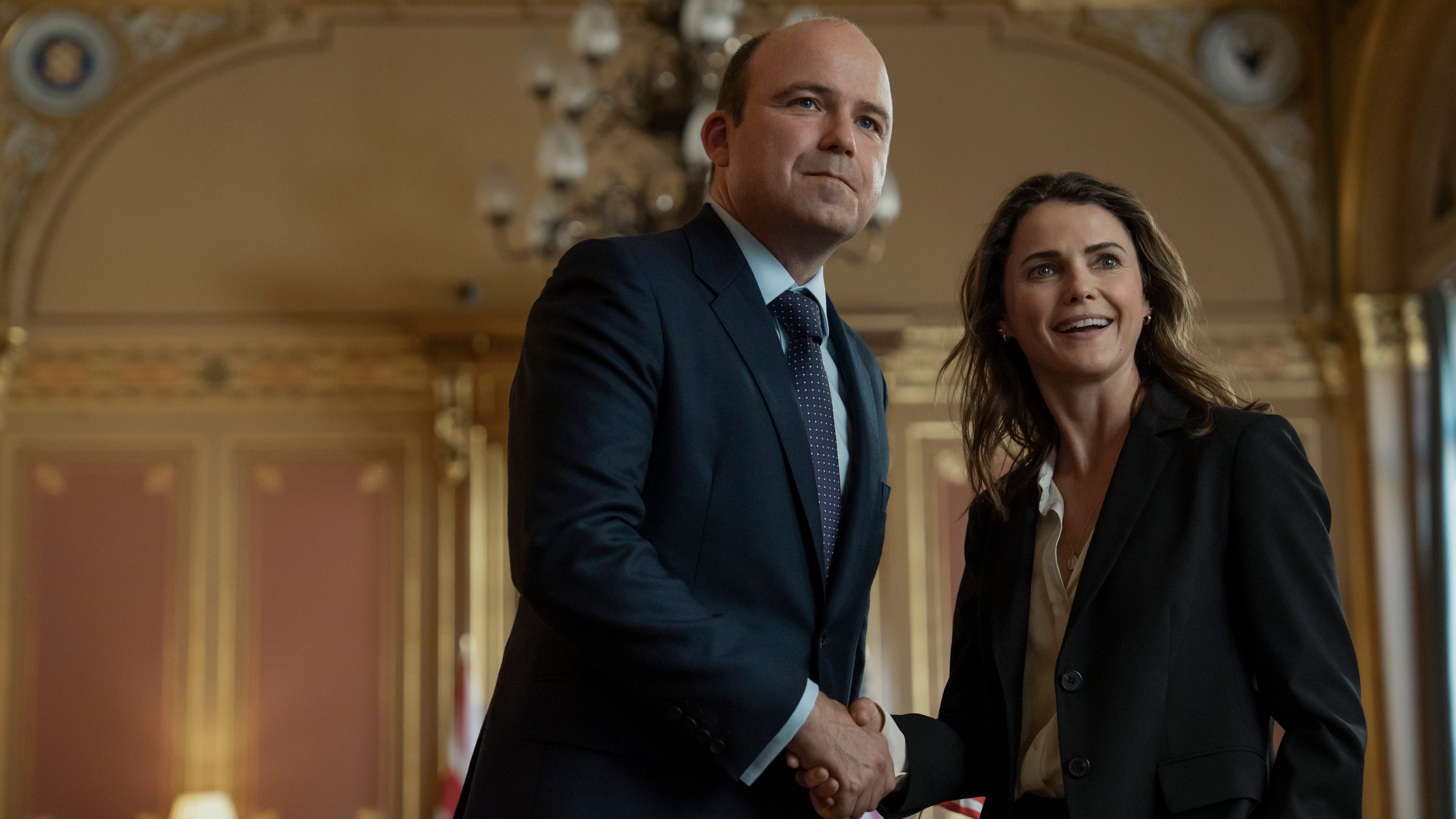 British Prime Minister Nicol and Kate smiling at something off camera as they shake hands in The Diplomat season 3.