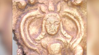 A close-up photo of the face of the ruler on the gold belt buckle.