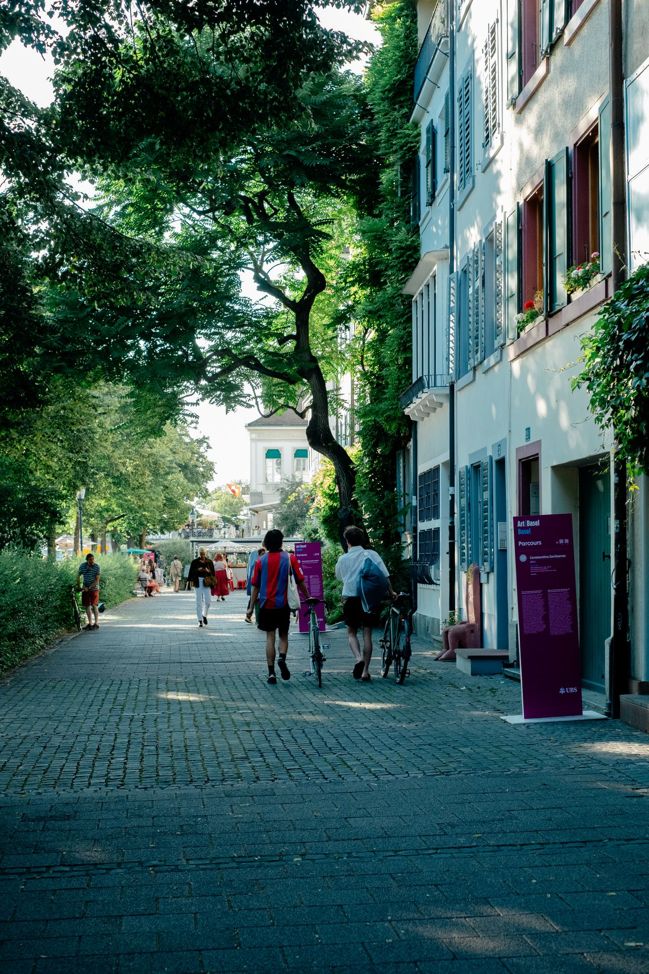 A series of lifestyle images depict people at leisure and play in a Swiss town bathing in sunshine, whether enjoying the weather near the river bank or abstract painting murals at an art fair.