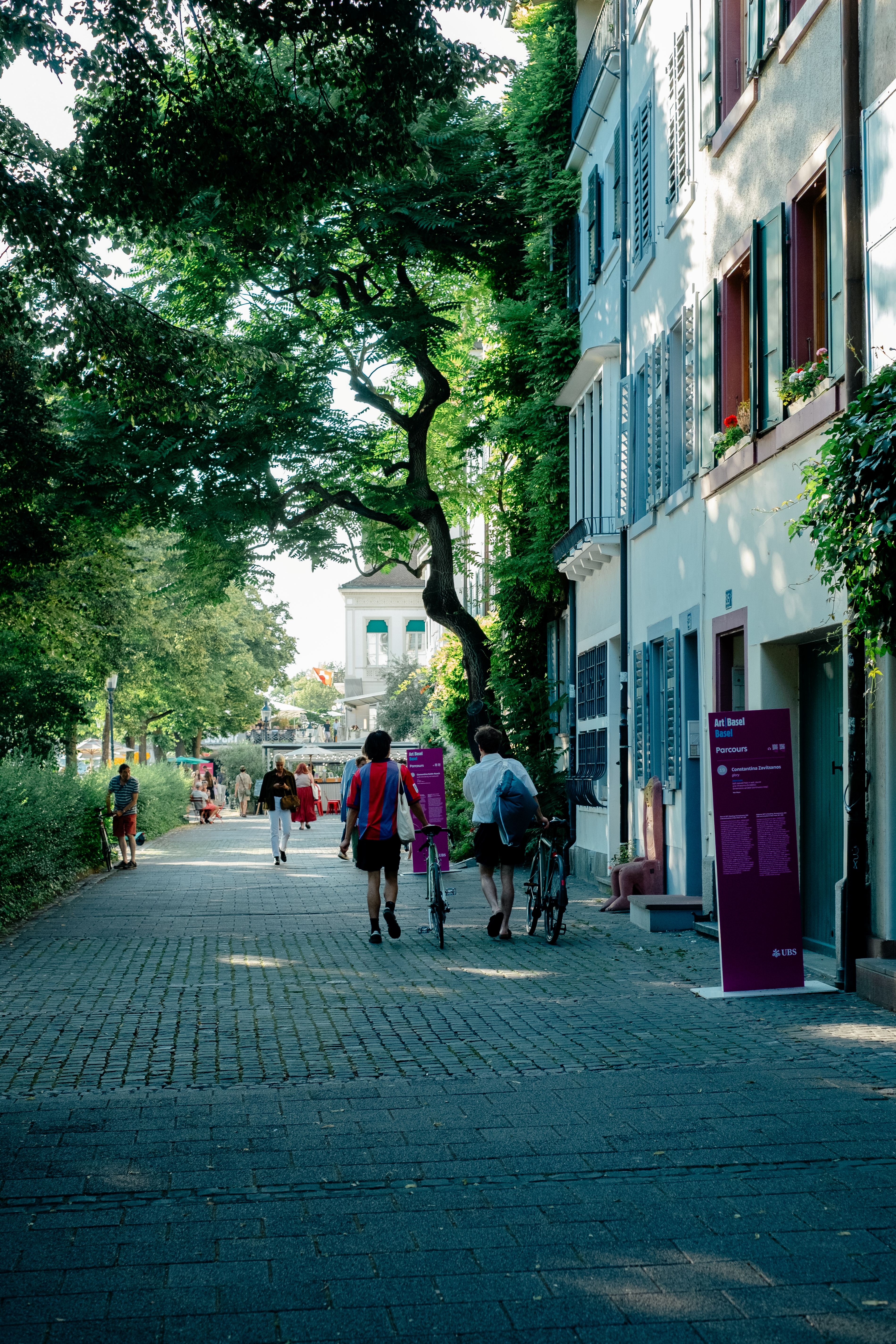 A series of lifestyle images depict people at leisure and play in a Swiss town bathing in sunshine, whether enjoying the weather near the river bank or abstract painting murals at an art fair.