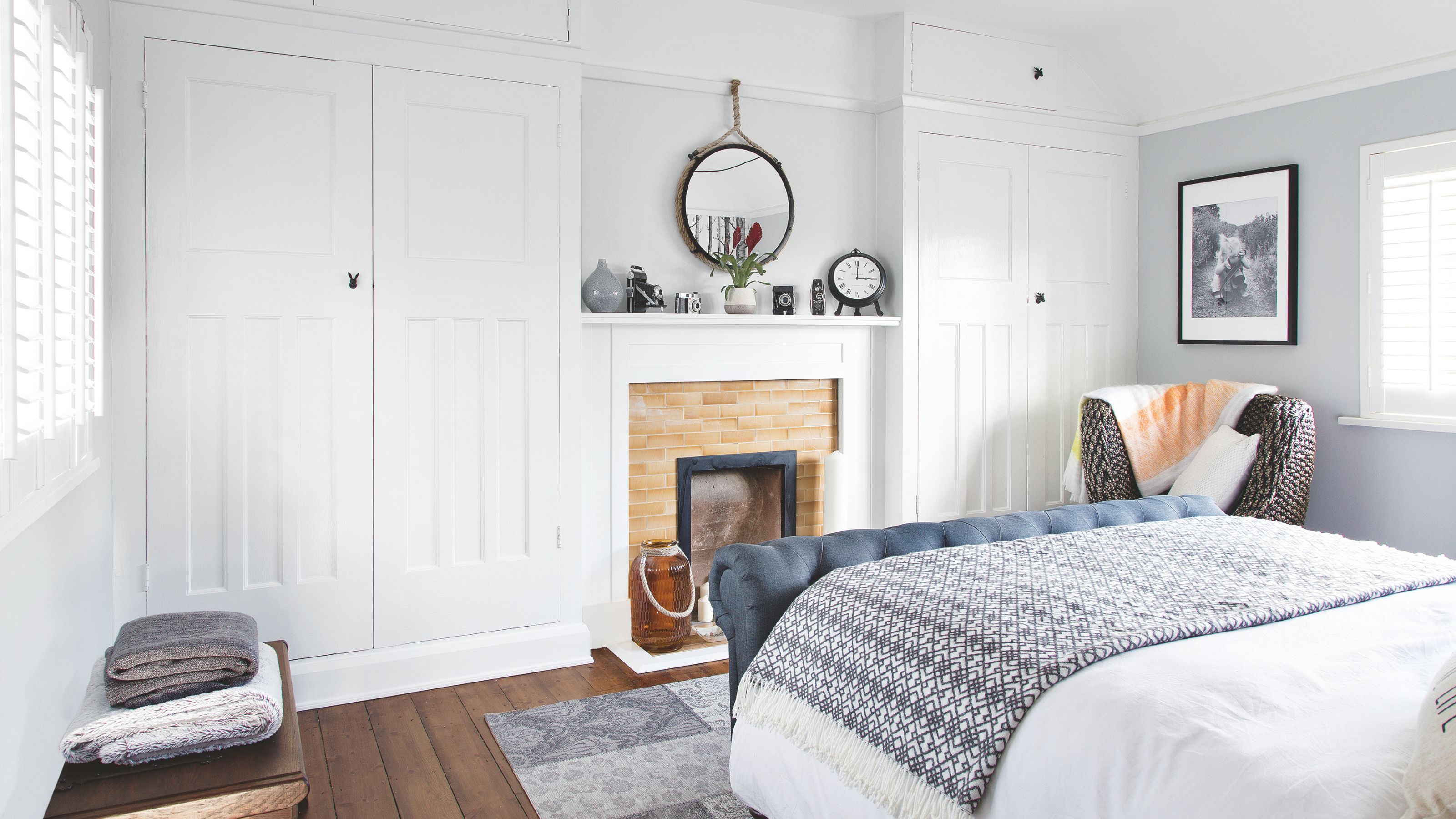 White painted bedroom with white fitted wardrobes either side of a small chimney and fireplace