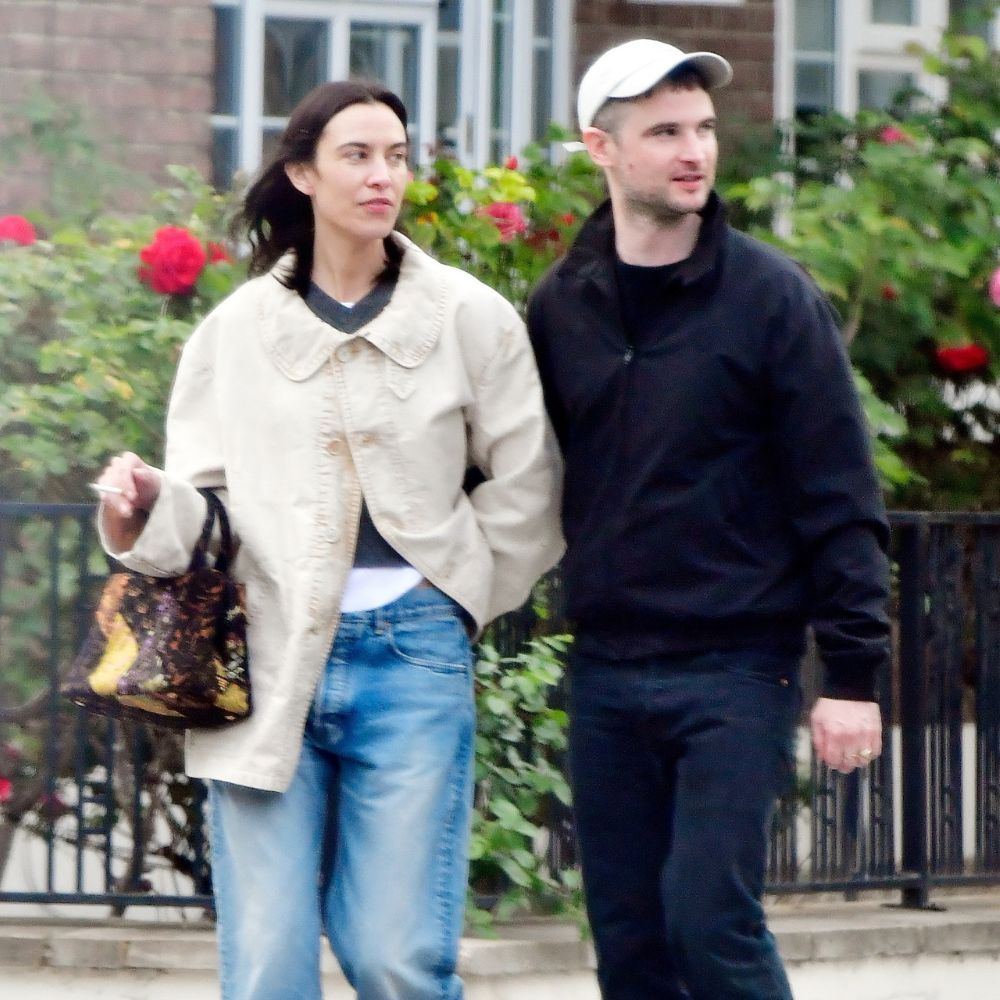 Alexa Chung walks down the street wearing blue jeans with black ballet pumps and a cream jacket.
