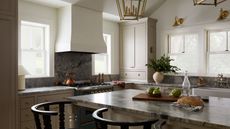 earthy neutral kitchen with large windows out to the lakeside view, a large plaster cooker hood, and blue marble countertops