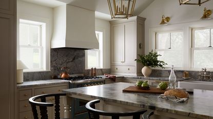 earthy neutral kitchen with large windows out to the lakeside view, a large plaster cooker hood, and blue marble countertops