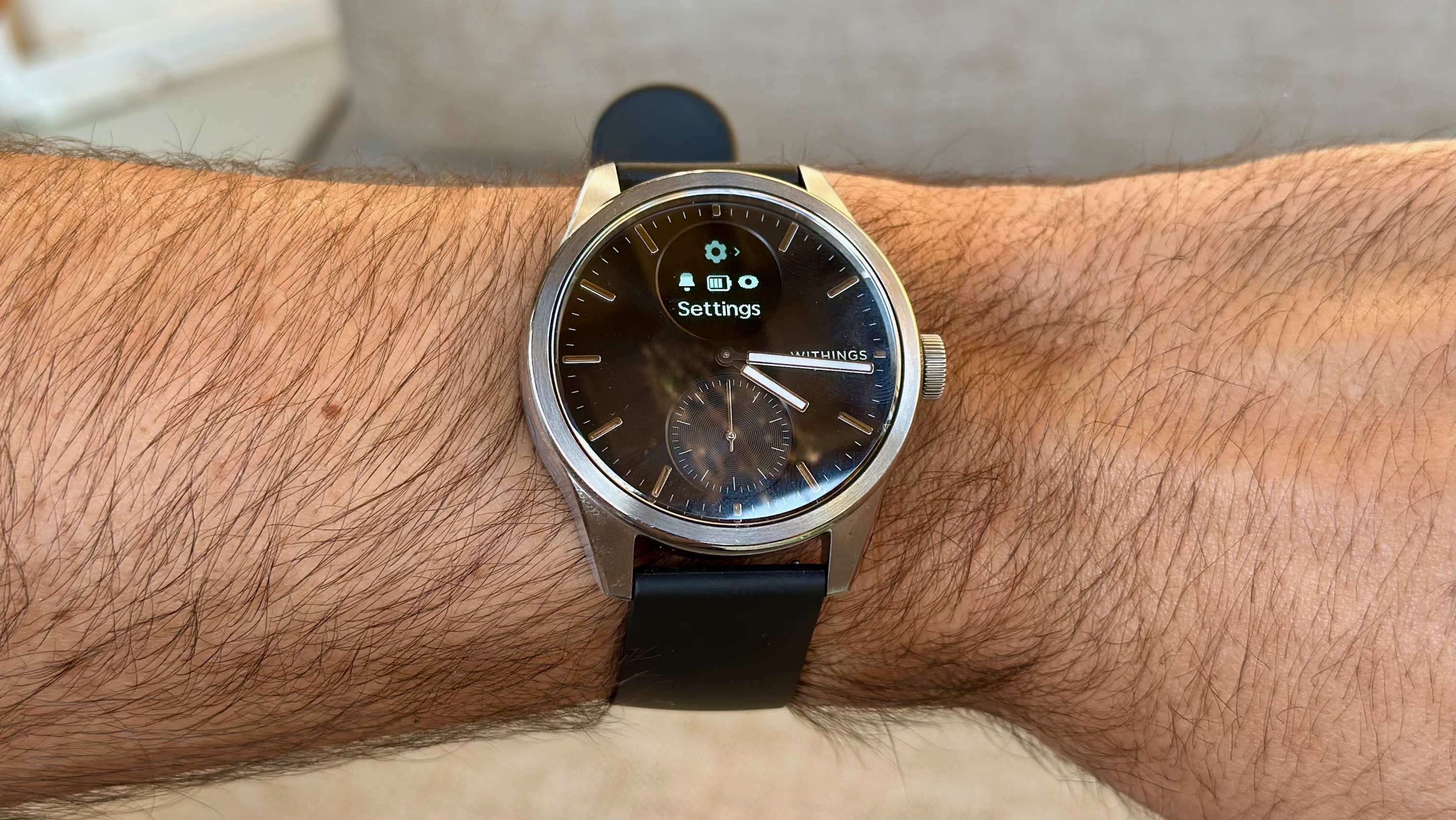 The Withings ScanWatch 2 on the author's wrist, showing the Settings menu on the small OLED screen.