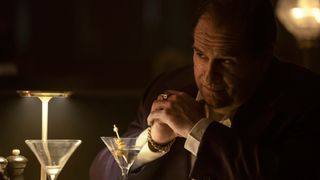 The Penguin (Colin Farrell) sitting at a dining table with a martini in the HBO Original "The Penguin"