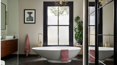 Bright bathroom with freestanding tub and large windows and mirrors, gold hardware and wooden undersink vanity