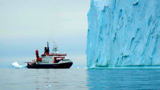A research vessel in front of a massive iceberg