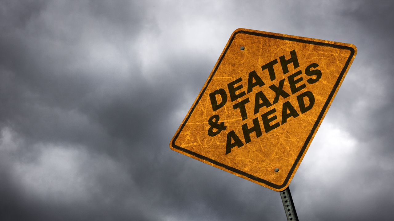 A caution sign against a stormy background reads &quot;death and taxes ahead.&quot;