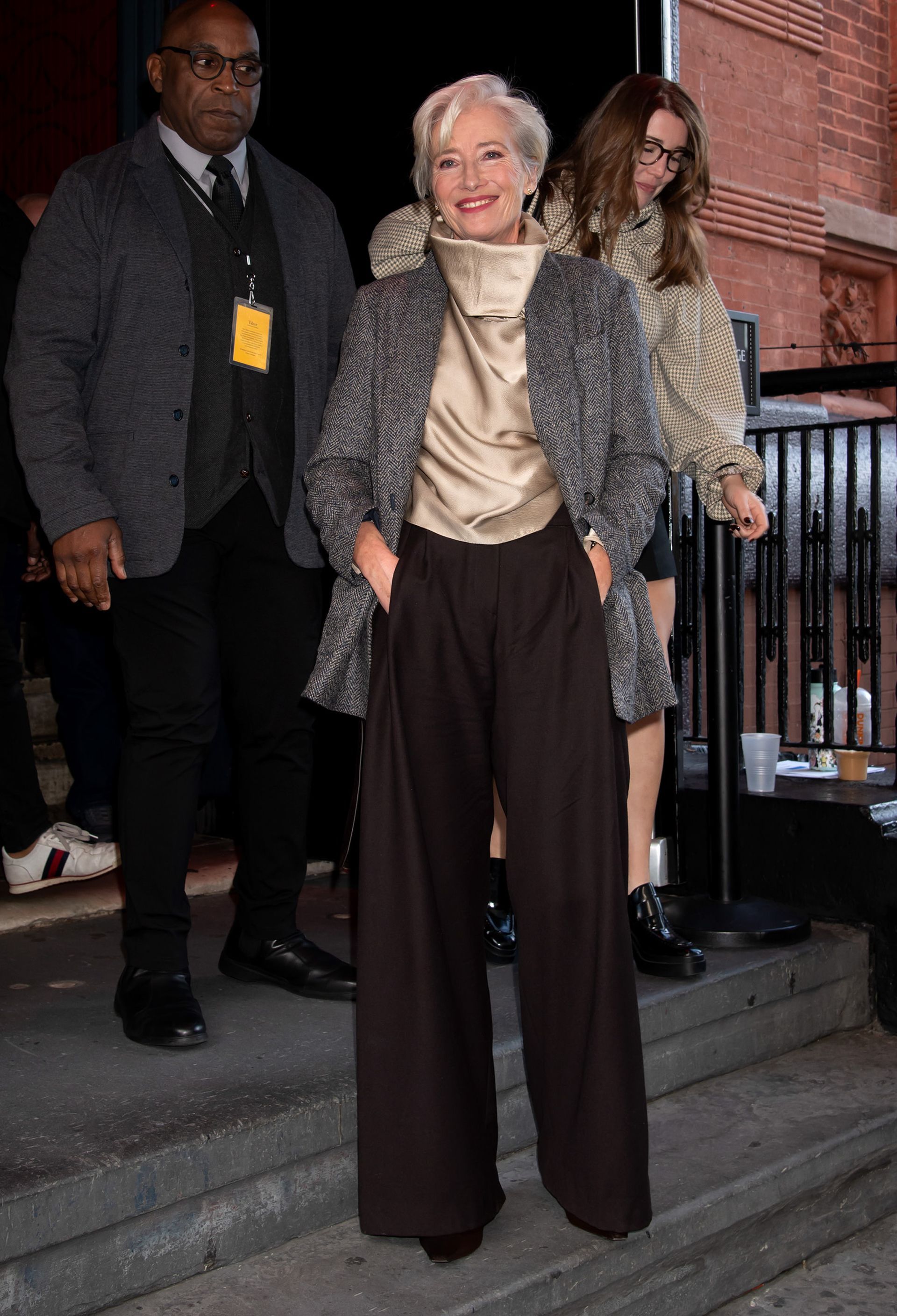 Emma Thompson wears a champagne satin blouse with brown wide-leg trousers and a grey blazer.