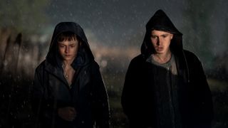 A still from the TV series A Murder at the End of the World showing the two lead characters walking at night wearing black hooded jackets.