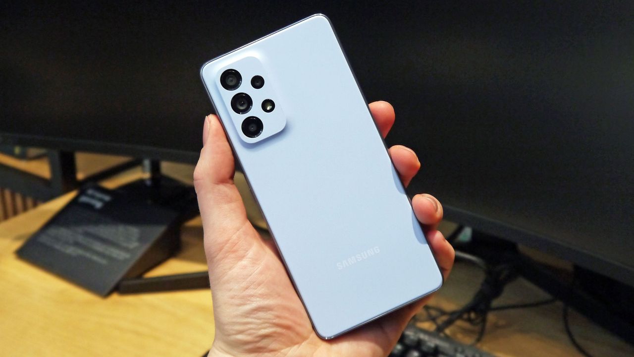 Samsung Galaxy A53 5G being held in a hand over a desk