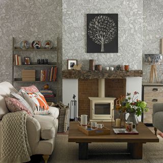Living room with cream sofa, grey patterned wallpaper, cream woodburner, wooden mantlepiece and coffee table
