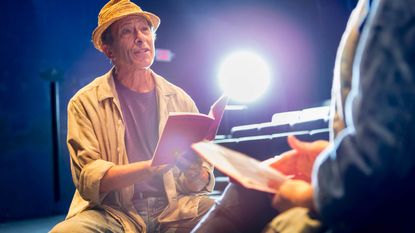 Senior actor on stage reading a script.