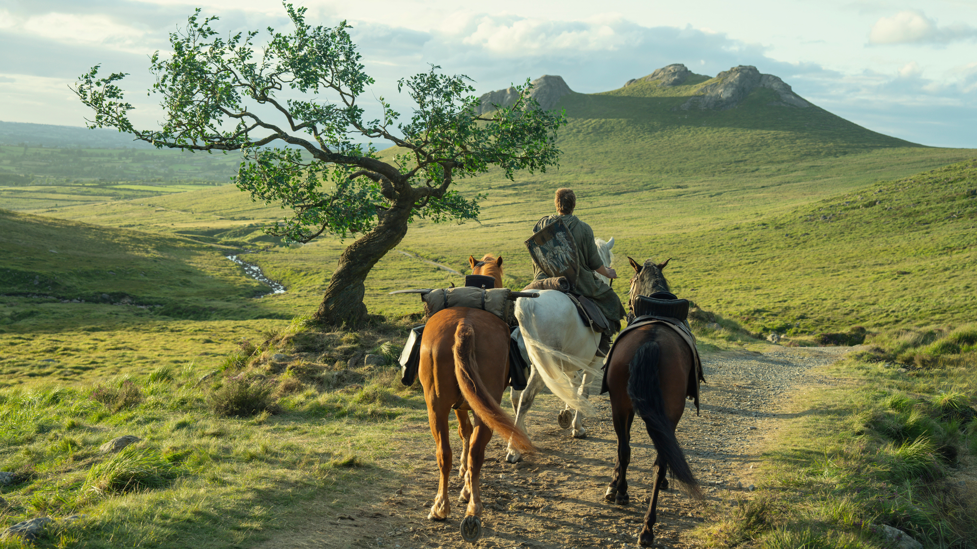 Ser Dunk (Peter Claffey) riding a horse away from the camera along a dirt road with two other horses in tow in a promotional still for &quot;A Knight of the Seven Kingdoms&quot;