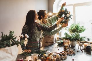 Two friends making Christmas wreaths together using fresh foliage.