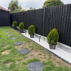 Garden with round pavers in grass, potted small trees by black fence and small lights in ground