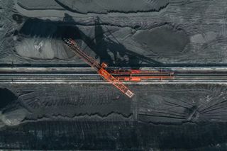 aerial view of red industrial equipment for mining on a fixed rail, amidst a grey landscape.