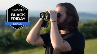 A person looking through the Celestron Nature DX 12x56 binoculars towards a black Space.com Black Friday deals badge, with trees in the background.