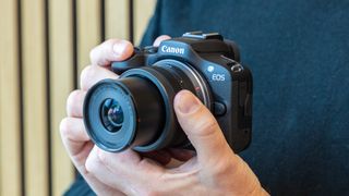 Canon EOS R100 being held by a man close to his chest