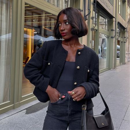 @aidabadji_ wears black skinny jeans with a boucle jacket and ballet flats while sitting on a pavement 