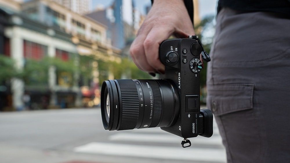 A hand holding a Sony camera with the Sigma 18-50mm f/2.8 DC DN lens attached