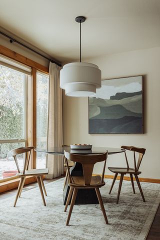 A dining room with a circular table, a pendant light and a framed painting